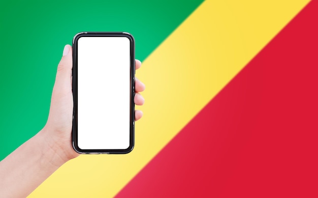 Nahaufnahme einer männlichen Hand, die ein Smartphone mit Leerzeichen auf dem Bildschirm auf dem Hintergrund der unscharfen Flagge des Kongo hält