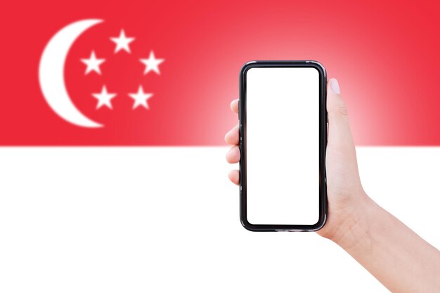 Nahaufnahme einer männlichen Hand, die ein Smartphone mit Leerzeichen auf dem Bildschirm auf dem Hintergrund der unscharfen Flagge Singapurs hält