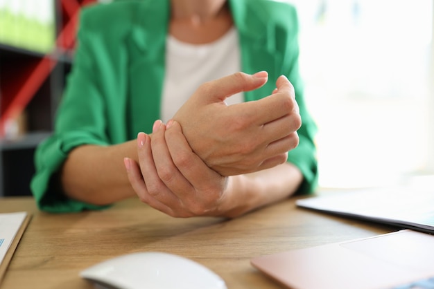 Nahaufnahme einer Managerin, die ihr schmerzhaftes Handgelenk hält, das durch lange Büroarbeit verursacht wurde