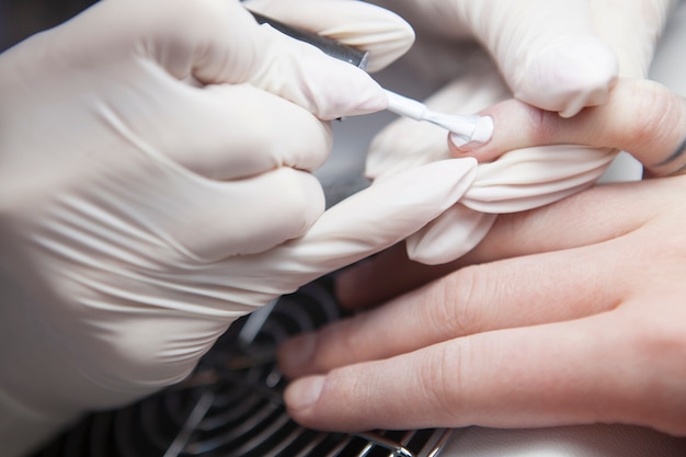 Nahaufnahme einer Maniküre, die weißen Nagellack auf die Nägel des Kunden aufträgt