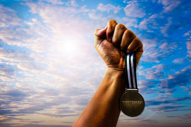 Nahaufnahme einer Medaille in der Hand gegen einen bewölkten Himmel bei Sonnenuntergang