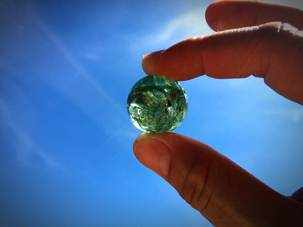 Nahaufnahme einer menschlichen Hand, die einen Marmorball gegen den blauen Himmel hält