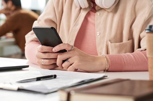 Nahaufnahme einer nicht erkennbaren Frau in Ringen, die am Schreibtisch sitzt und die Nachricht am Telefon überprüft