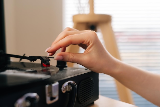 Nahaufnahme einer nicht wiederzuerkennenden jungen Frau, die eine Schallplatte in ein altes Grammophon legt und anfängt, Retro-Musik zu hören