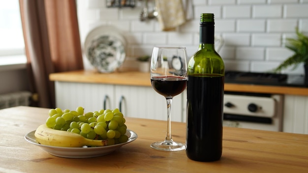Nahaufnahme einer offenen Flasche Wein und eines Glases Wein mit Früchten auf dem Teller auf dem Tisch in der Küche Konzept der Datierung