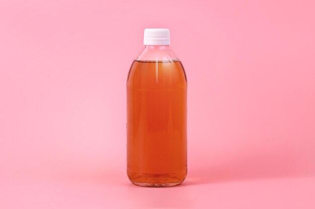Nahaufnahme einer orangefarbenen Flüssigkeit in einer Plastikflasche vor rosa Hintergrund