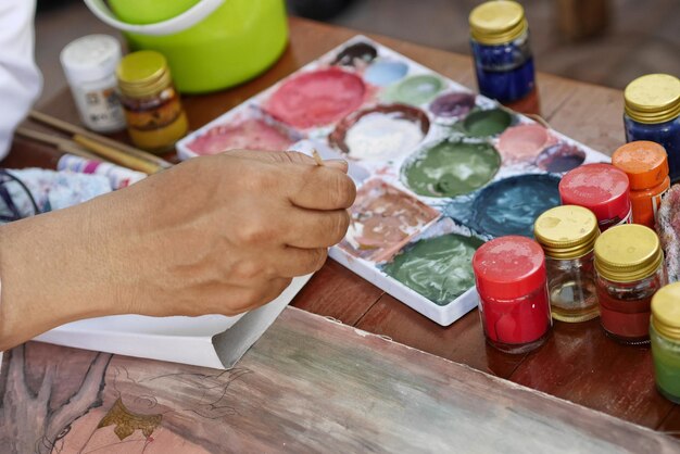 Foto nahaufnahme einer person, die einen pinsel über einer palette am tisch hält