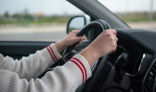 Nahaufnahme einer Person Hände, die das Lenkrad eines Autos halten, während auf einer Straße fahren