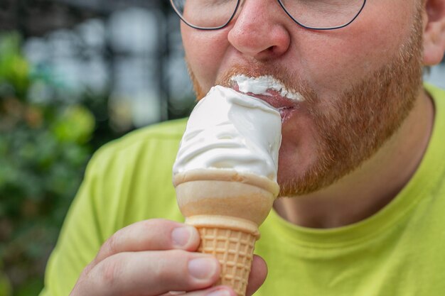 Nahaufnahme einer Person in einem lime-grünen Hemd, die Vanille-Eis von einem Kegel isst, der Vergnügen darstellt