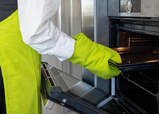 Nahaufnahme einer Person mit grünen Handschuhen, die ein Metallblech in den Ofen stellt, horizontales Bild