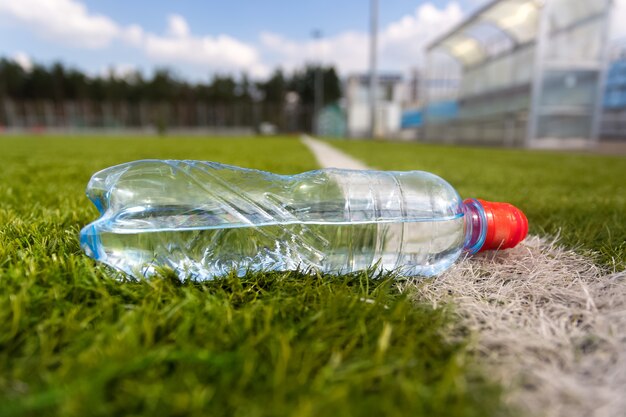 Nahaufnahme einer Plastikflasche Wasser, die auf dem Rasenfußballplatz liegt