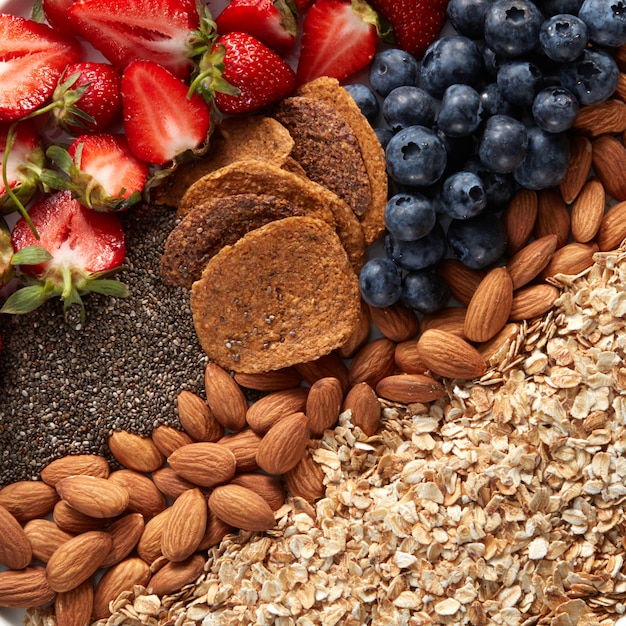 Nahaufnahme einer Reihe von Zutaten, Haferflocken, Müsli, Mandeln, Snacks, Blaubeeren und Erdbeeren halbiert die Draufsicht. Gesundes Vitaminfrühstück