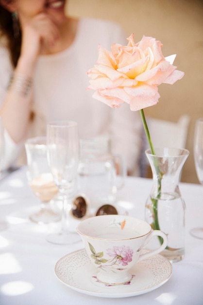 Nahaufnahme einer Rose in einer Vase auf einem Tisch mit Tasse und Untertasse und Gläsern