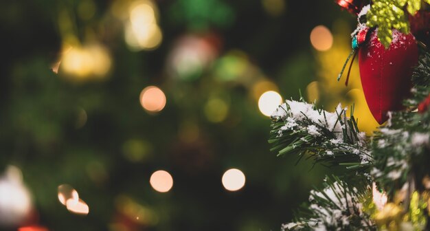 Nahaufnahme einer roten Geschenktüte, die mit Kunstschnee auf grünem Weihnachtskieferzweig und Blättern in der traditionellen Festnachtsveranstaltung am Weihnachtsabend im Wohnzimmer hängt.