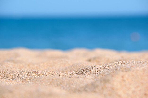 Nahaufnahme einer sauberen gelben Sandoberfläche, die den Strand am Meer mit blauem Meerwasser im Hintergrund bedeckt Reise- und Urlaubskonzept