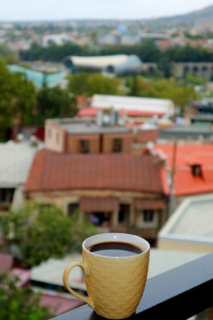 Nahaufnahme einer Schale heißen Kaffees auf dem Balkon mit undeutlicher Stadt-Ansicht in den Hintergrund