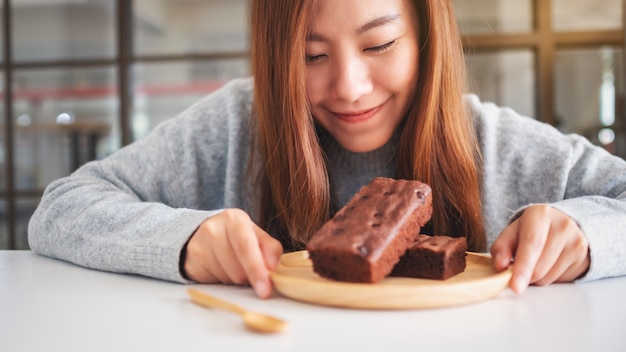 Nahaufnahme einer schönen asiatischen Frau, die Brownie-Kuchen in Holzplatte hält und betrachtet