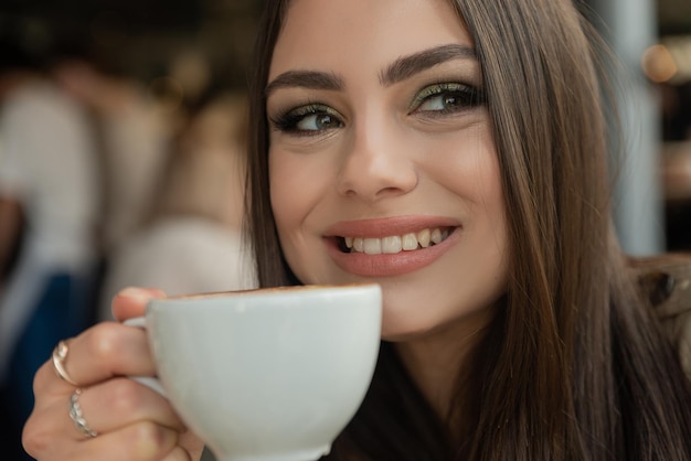 Nahaufnahme einer schönen brünetten Frau mit einer Tasse Kaffee im Café, die lächelt und zur Seite schaut