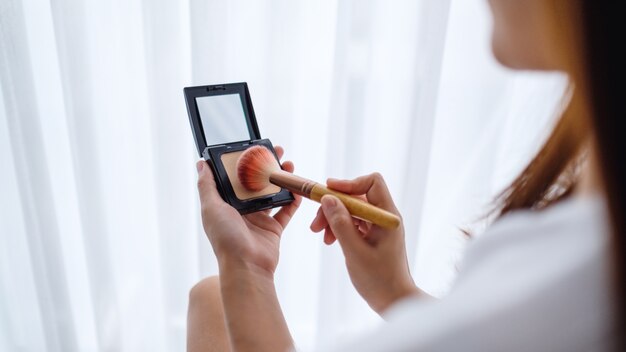 Nahaufnahme einer schönen Frau, die Make-up-Pulver mit Pinsel im Schlafzimmer aufträgt