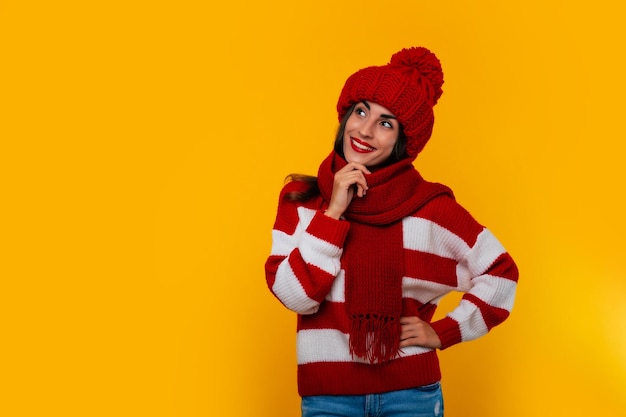 Foto nahaufnahme einer schönen glücklichen brünetten frau in roter wintermütze und schal und posiert auf gelbem hintergrund