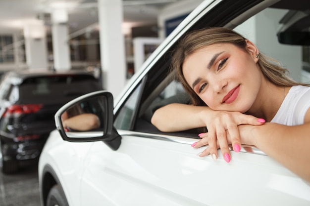 Nahaufnahme einer schönen glücklichen Frau, die freudig lächelt und in ihrem neuen Auto im Autohaus sitzt sitting