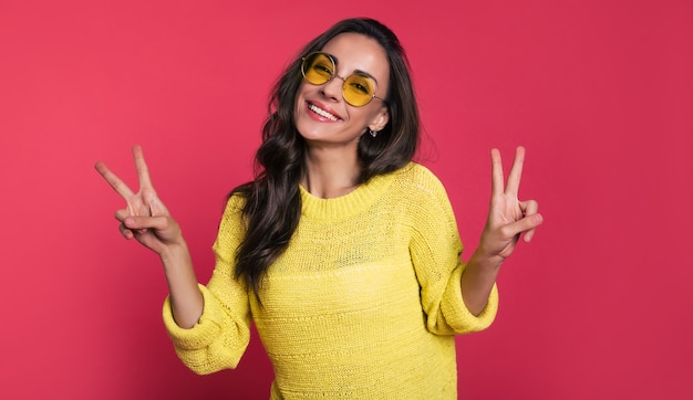 Nahaufnahme einer schönen jungen Frau in gelbem Outfit und Sonnenbrille, die mit geschlossenen Augen lacht und posiert