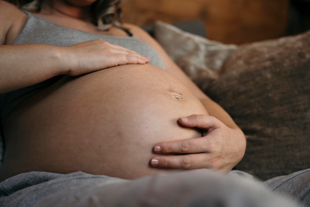 Nahaufnahme einer schwangeren Frau, die es sich auf ihrem Sofa gemütlich macht und ihren Bauch wiegt