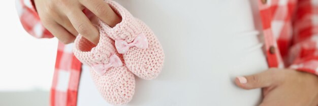 Nahaufnahme einer schwangeren Frau, die rosa Babyschuhe auf dem Bauch hält, glückliche und gesunde Schwangerschaft