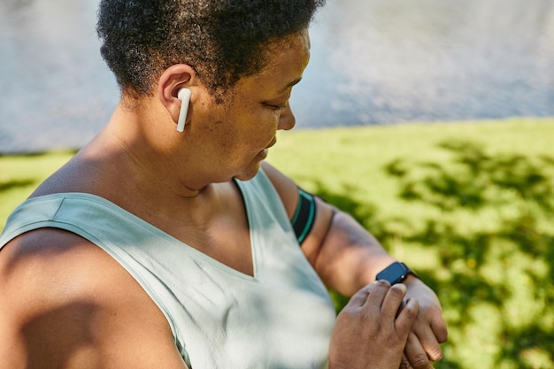 Nahaufnahme einer schwarzen Frau, die Smartwatch überprüft, während sie im Freien mit Musik läuft