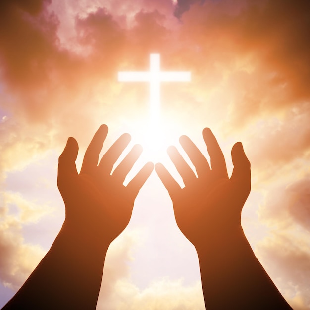 Nahaufnahme einer Silhouette-Hand gegen Sonnenlicht Kreuz und Himmel