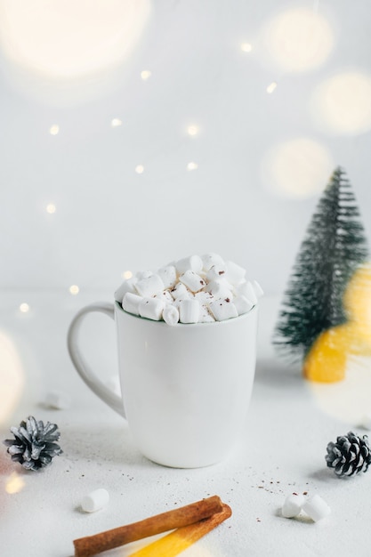 Nahaufnahme einer Tasse mit Kakao und Mrashmallow auf dem Hintergrund eines Weihnachtsbaums aus Kegeln von Zimtstangen auf weißem Hintergrund