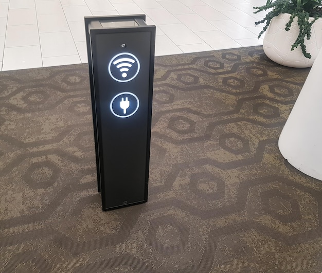 Nahaufnahme einer Telefonladestation über USB und einer Wi-Fi-Zone am Flughafen oder Supermarkt, Pflanzen in der Nähe in weißen Blumentöpfen