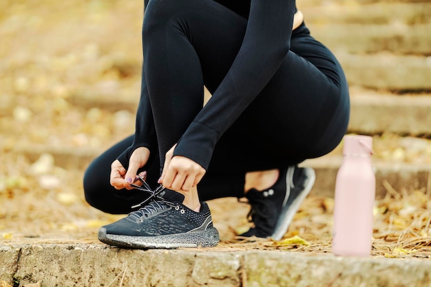 Nahaufnahme einer unerkennbaren Sportlerin, die Schnürsenkel in der Natur bindet