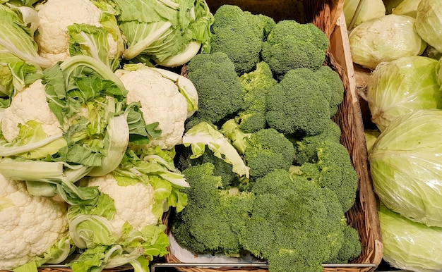 Nahaufnahme einer Vitrine mit frischem Weißkohl, Blumenkohl und Brokkoli in Weidenkörben, Hintergrund von Gemüse auf dem Markt
