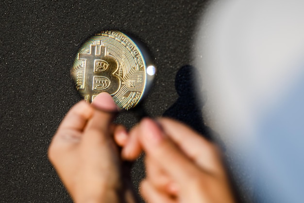 Nahaufnahme einer weiblichen Hand, die eine Lupe hält und durch sie auf Bitcoin schaut Das Konzept der Forschung und Untersuchung des Kryptowährungsmarktes