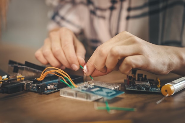 Nahaufnahme einer weiblichen Hand ist die Reparatur elektronischer Geräte durch Lötkolben auf dem Tisch.