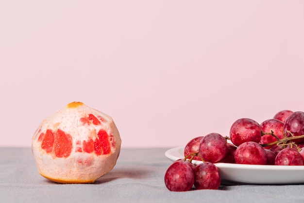 Nahaufnahme einer Weintraube und einer geschälten Grapefruit auf einem rosa Hintergrund. Minimalistisches Stillleben mit Speicherplatz für Ihren Text.