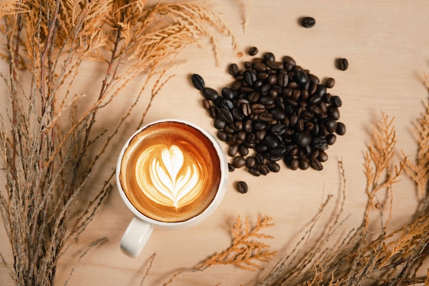 Nahaufnahme einer weißen Kaffeetasse mit heißem Cappuccino mit herzförmiger Latte Art und Blumen