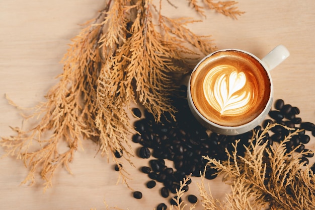 Nahaufnahme einer weißen Kaffeetasse mit heißem Cappuccino mit herzförmiger Latte Art und Blumenessen und