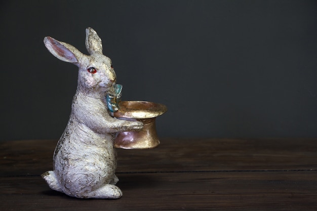 Nahaufnahme einer weißgoldenen Statuette eines Osterhasen, der einen leeren Hut, Osternhintergrund oder -konzept, selektiven Fokus hält