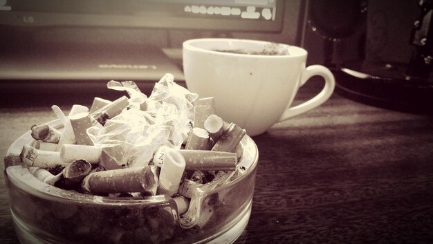 Nahaufnahme einer Zigarette in einem Aschenbecher neben einer Kaffeetasse auf dem Tisch