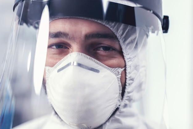 Nahaufnahme eines abgenutzten Medizintechnikers mit Gesichtsmaske und PSA-Anzug. Überarbeiteter Forscher in Schutzanzug gegen Infektion mit Coronavirus während der globalen Epidemie.
