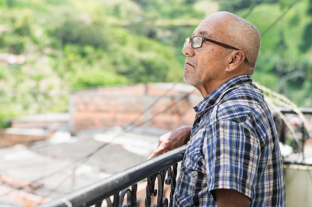 Nahaufnahme eines älteren Latino-Mannes, der auf dem Balkon seines Hauses steht und in den Himmel blickt