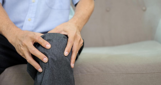 Nahaufnahme eines älteren Mannes, der unter Knieschmerzen leidet und auf dem Sofa sitzt