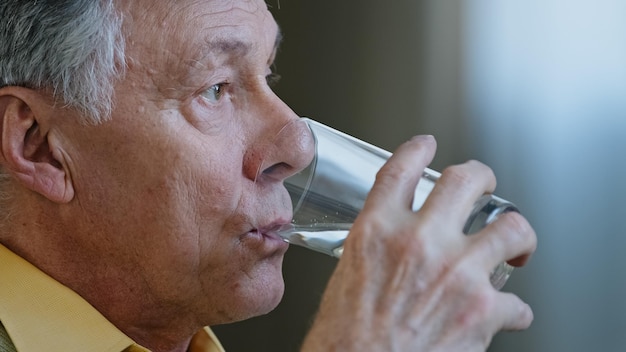 Nahaufnahme eines älteren, reifen, kaukasischen Mannes, der wegschaut und ein Glas sauberes, stilles Wasser hält