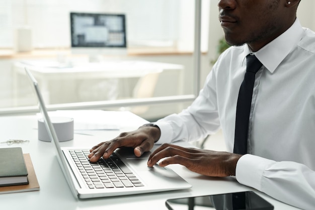 Nahaufnahme eines afrikanisch-amerikanischen Geschäftsmannes im weißen Hemd, der online am Laptop im Büro arbeitet