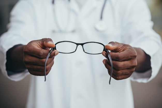 Nahaufnahme eines afroamerikanischen Arztes bietet dem Patienten eine Brille an, ein Augenarzt verkauft eine Brille im Geschäft