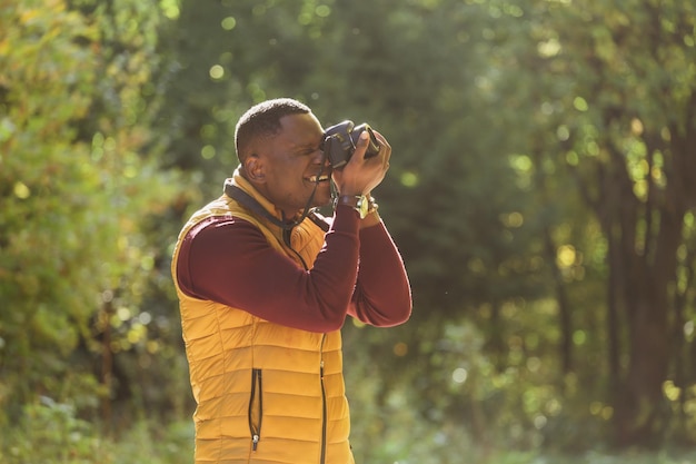 Nahaufnahme eines afroamerikanischen Fotografen, der ein Foto mit einer Fotokamera auf einer grünen Parkkopie der Stadt macht