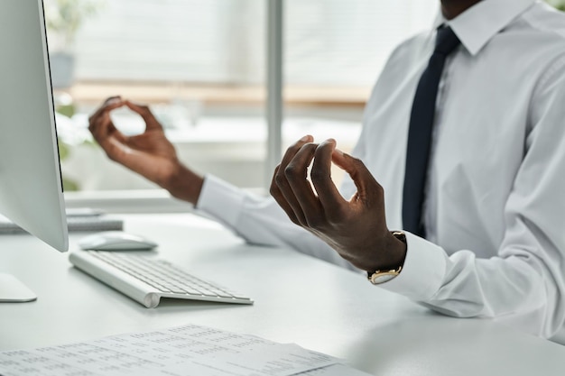 Nahaufnahme eines afroamerikanischen Geschäftsmannes, der während des Arbeitstages an seinem Arbeitsplatz meditiert und sich entspannt