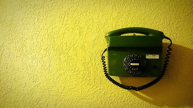 Nahaufnahme eines alten Telefons an einer gelben Wand